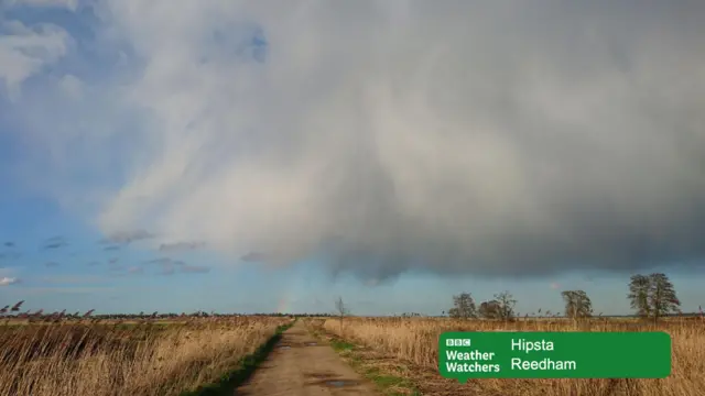 
          Stormy clouds over open countryside, with the hint of a rainbow
        