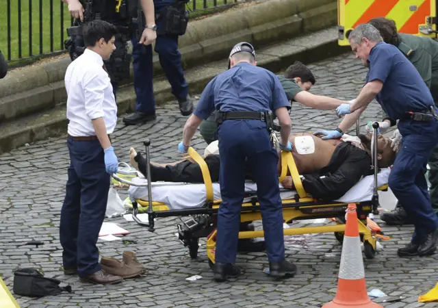 
          A man is treated by emergency services, as knives lie on the floor, with police looking on at the scene
        