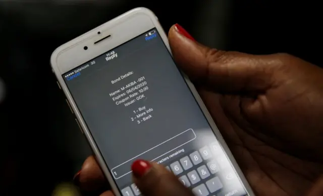 
          A delegate uses her mobile phone to buy a M-Akiba bond during the launch of the first mobile-phone-based government bond at the Treasury building in Nairobi, Kenya March 23, 2017.
        