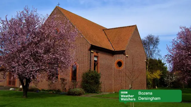 A brick house with pink blossom trees in the gardern