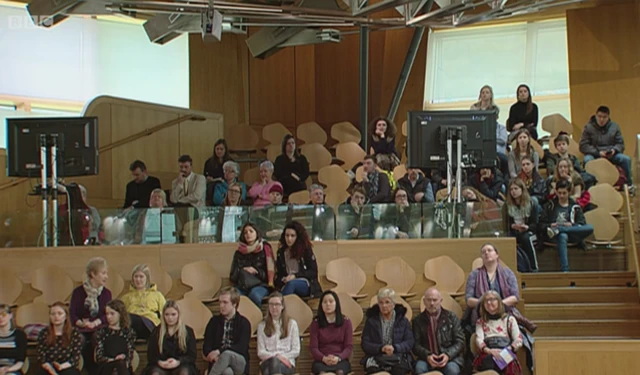 Members of the public watch on from the gallery