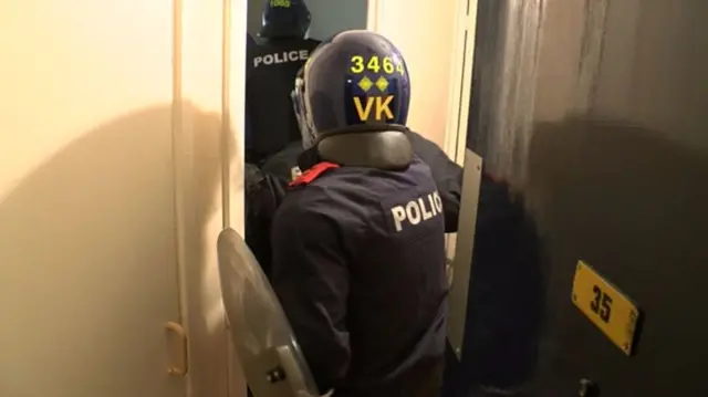 Police officers enter property, wearing visors and helmets