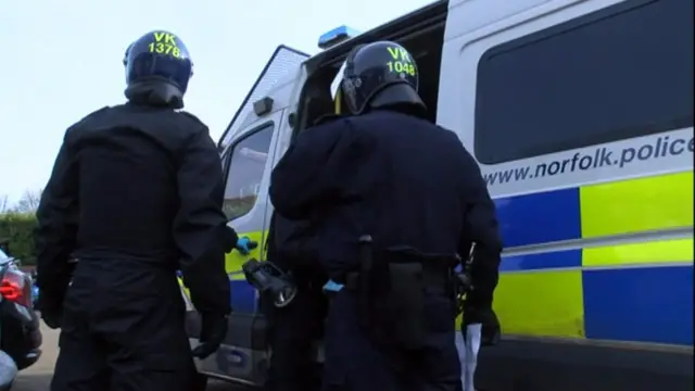 
          Police officers in helmets and visors stand by police vehicle
        