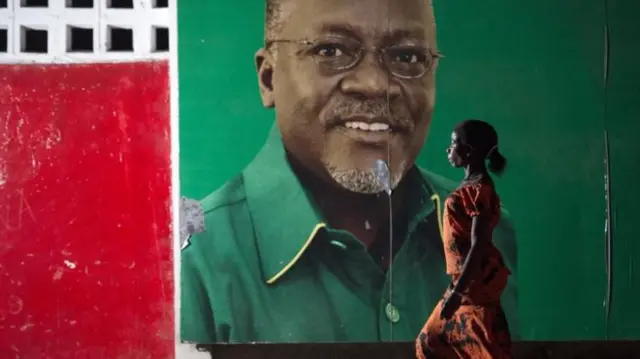 Woman walks past Magufuli poster on the wall