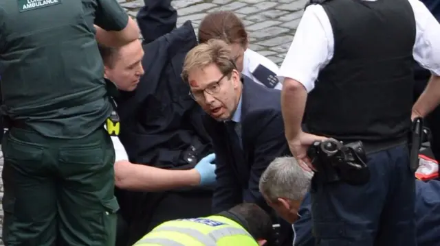 
          Conservative MP Tobias Ellwood helps emergency services attend to a police officer outside the Palace of Westminster
        