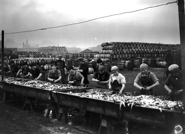 
          Black and white photo showing women at work on a catch of herring at Lowestoft in 1921
        