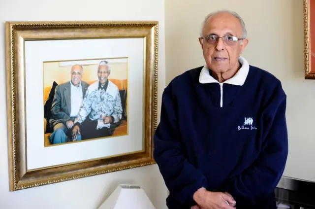 
          This file photo taken on July 16, 2012 shows 82-year-old Ahmed Kathrada, anti-apartheid activist and close friend of former South African President Nelson Mandela posing next to a picture of himself with Nelson Mandela in his house in Johannesburg
        