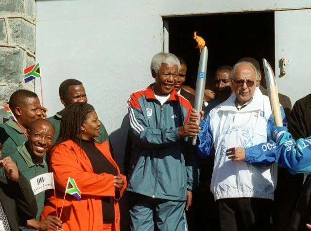 
          this file photo taken on June 12, 2004 shows Former South African President Nelson Mandela (C) and former political prisoner Ahmed Kathrada (R) hold the Olympic Flame at the entrance to the former maximum security prison on Robben Island, Cape Town
        