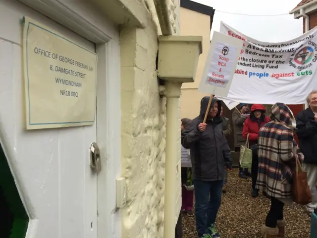 
          Protestors with banners outside the door of George Freeman's office in Wymondham
        