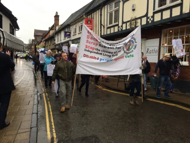 
          Disability campaigners holding banners as they march through Wymondham town centre
        