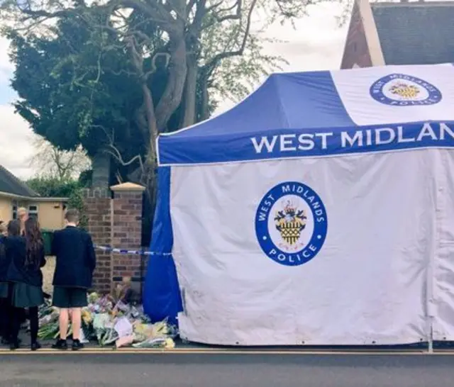 School children gather near floral tributes and police tent