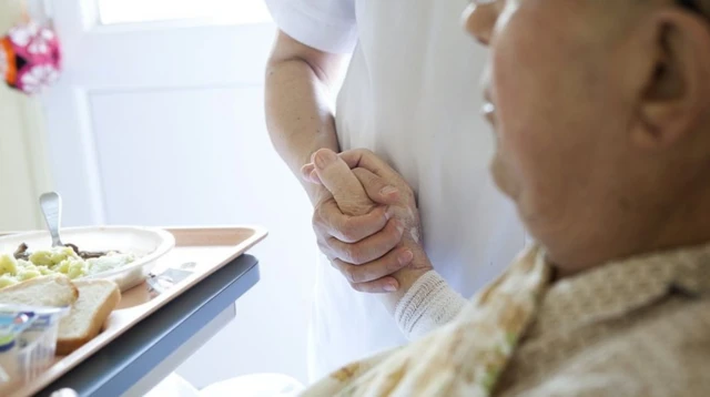 Man in hospital bed with nurse holding his hand