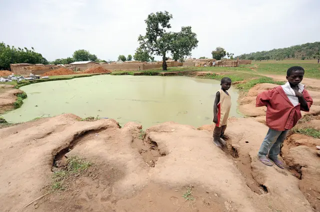 
          Two young boys stand in front of a pond infected with lead poison at Dareta village, Anka district in Zamfara State
        