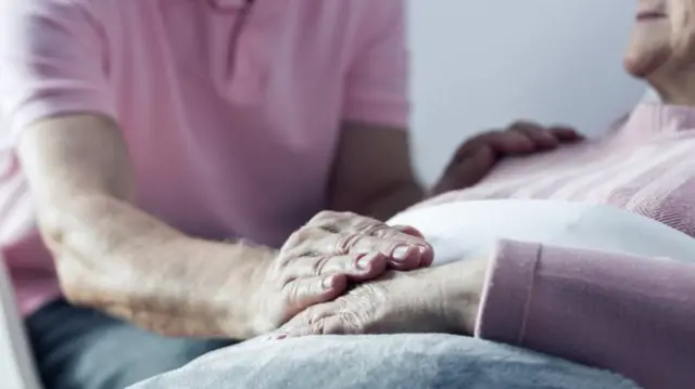 Elderly woman in bed with man holding her hand