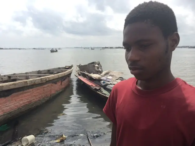 Nathaniel Loko stands by a small boat on the shore