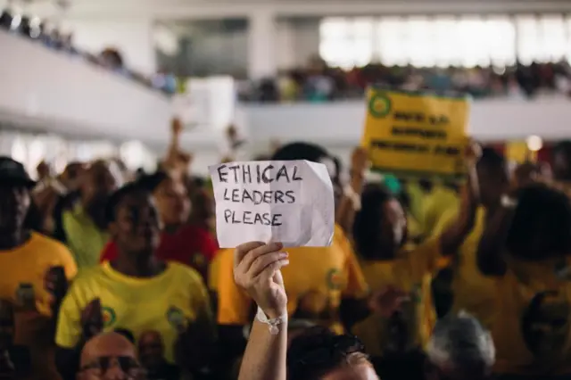 
          A woman holds a placard as South African ruling Party African National Congress Youth League members shout slogans in support of South African President Jacob Zuma as sacked finance minister Pravin Gordhan speaks at a memorial service held in Durban in honour of anti-apartheid icon Ahmed Kathrada on April 9, 2017 in Durban.
        