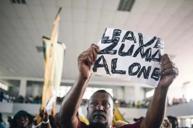 
          South African ruling Party African National Congress Youth League member holds up a sign in support of South African President Jacob Zuma as sacked finance minister Pravin Gordhan speaks at a memorial service held in Durban in honour of anti-apartheid icon Ahmed Kathrada on April 9, 2017 in Durban.
        