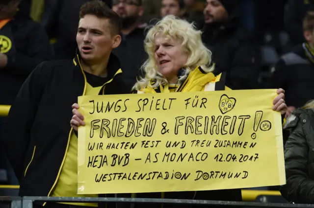 A fan holds a sign reading "Guys play for peace and freedom"