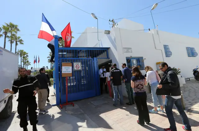 people queuing in the sun outside distinctive white North African building