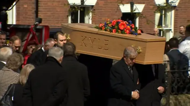 Kyle's coffin, with red and blue flowers, being carried into church by pallbearers