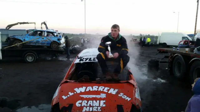 Kyle Warren sitting on the bonnet of a red banger car