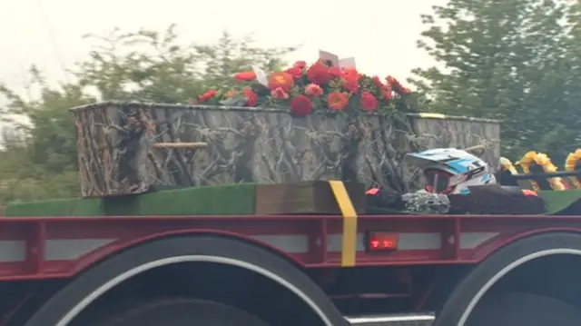 Coffin, with flowers, on lorry