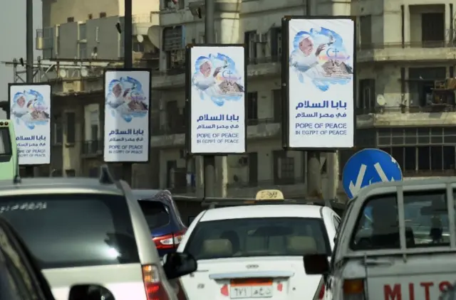 Cars drive past welcome banners bearing a portrait