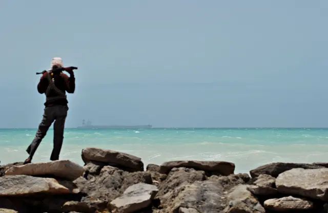 Somali pirate stands on the rocks looking out from the shore