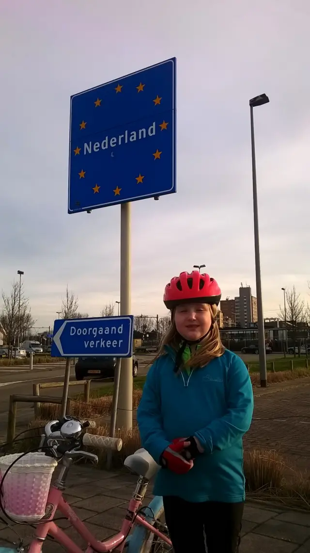 
          Georgia, in blue top and wearing a cycle helmet, stands besides her pink bike
        