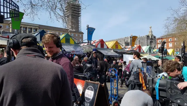 
          Stepeh Merchant, in the background, with film crew in front of Norwich market
        