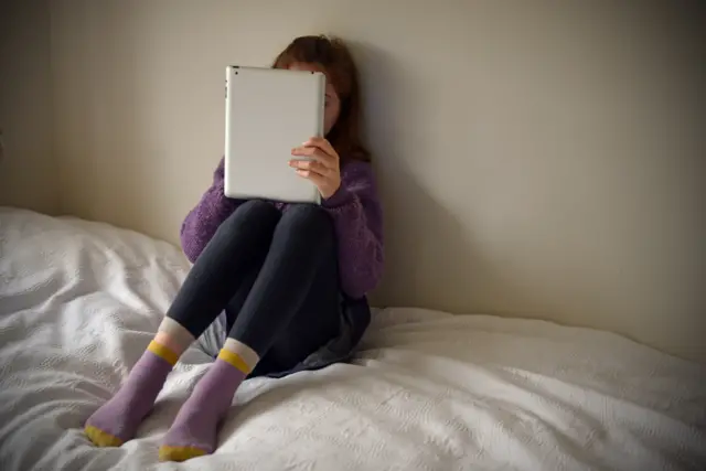 Young girl sitting on a bed, with computer tablet in hand