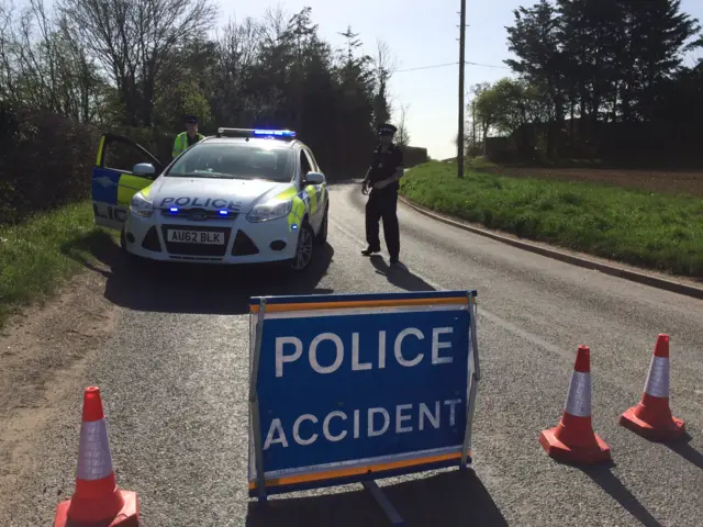 
          Two police officers standing by a police vehicle and police accident sign
        