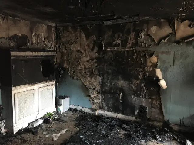 
          A fire-damaged room in the house, showing black walls and flooring
        