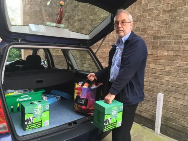 Alan Smith, standing at the open boot of a car, with boxes of milk cartons and a shopping bag