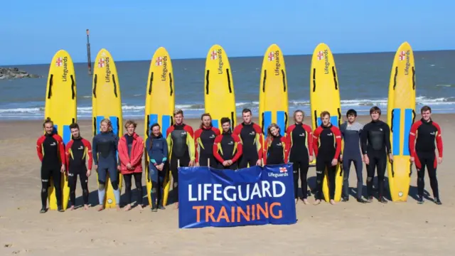 Lifeguards lined up with their surf boards on a beach