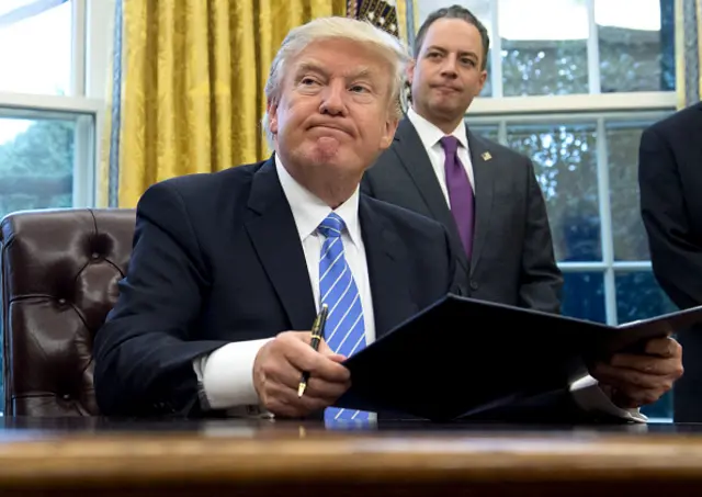 US President Donald Trump signs an executive order as Chief of Staff Reince Priebus looks on in the Oval Office of the White House in Washington, DC, on 23 January, 2017.