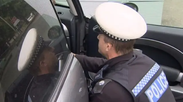 Police officer crouched down by open car door