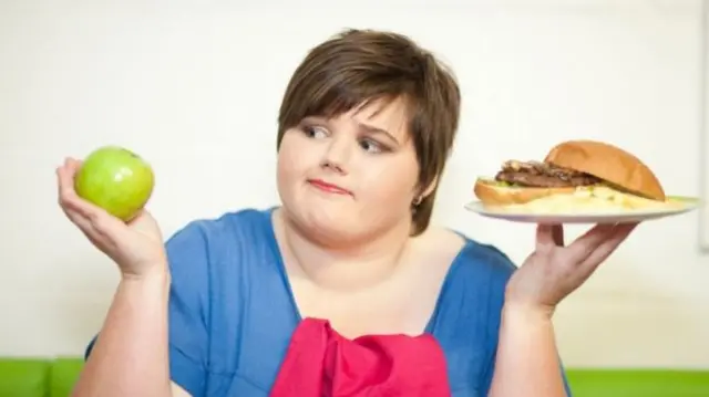 Woman with apple in one hand and hamburger in the other