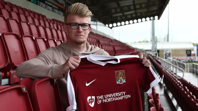 New Cobblers signing, George Smith, holding a club shirt.