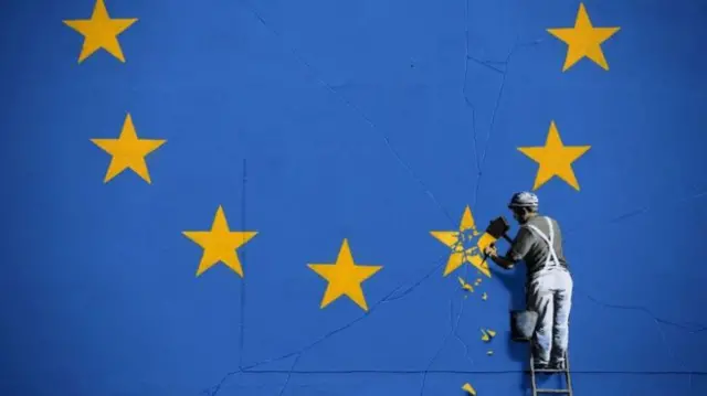 Man chipping off EU emblem on wall