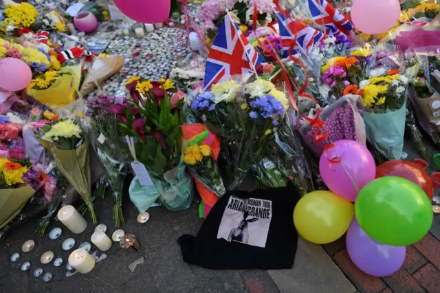 Flowers, messages and candles are pictured alongside a t-shirt from Ariana Grande's Dangerous Woman tour in St Ann's Square in Manchester