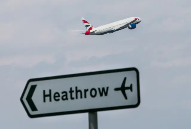 A BA plane takes off above a sign pointing to Heathrow airport