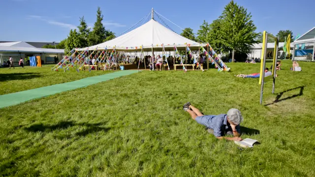 Woman reading on the grass in front of tent