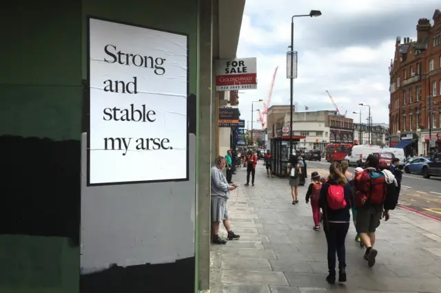 A poster by artist Jeremy Deller, in response to Prime Minister Theresa May, is pasted on to a wall in Camden