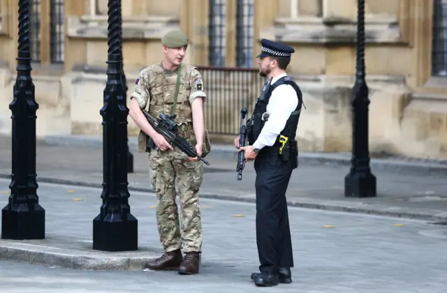 A police officer talks to a soldier outside the houses of parliament