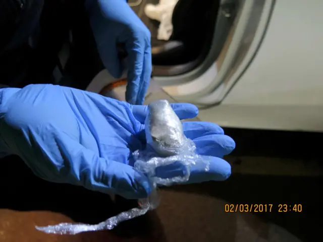 A gloved hand holding packets of drugs