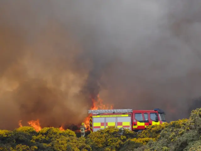 Close shot of fire engine with flames and smoke behind