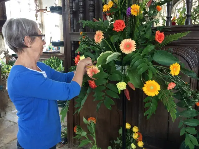 A woman wearing blue works on a floral display