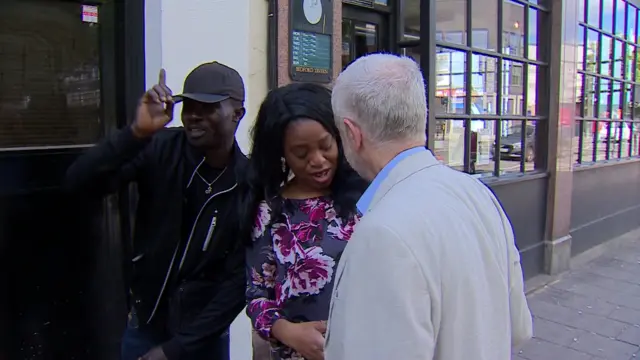 Jeremy Corbyn shakes hands with a woman as a man gesticulates in the background