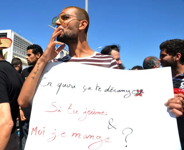 A Tunisian protester smokes a cigarette and holds a placard reading in French 'Why is it bothering you? If you fast and I eat?' during a demonstration for the right to eat and smoke in public during the Muslim dawn-to-dusk fasting month of Ramadan, on June 11, 2017, in Tunis.